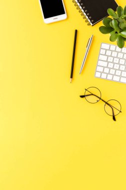 Sarı arka planda iş aksesuarları ve kopyalama alanı olan zarif bir çalışma alanı. Ofis masaüstü