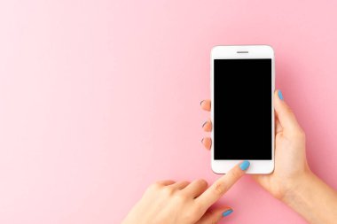 Pembe arka planda boş ekranlı akıllı telefon kullanan kadın ellerinin yukarıdan çekimleri. Üst görünüm