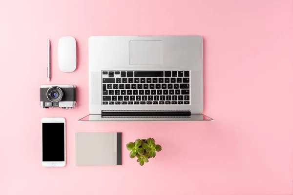 Modern workspace concept with laptop and business accessories on pink background with copyspace. Office desktop. Top view