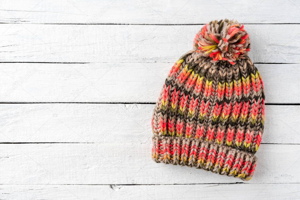 Overhead shot of colourful winter hat with pompon on white wooden background with copyspace