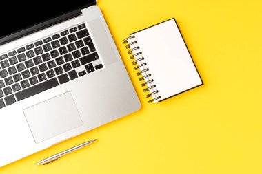 Ofis masaüstü dizüstü bilgisayarı, dizüstü bilgisayarı ve sarı arka planda, kopya alanı olan bir kalem. Modern işyeri