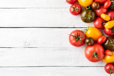 Telif alanı olan beyaz ahşap masadaki çeşitli domateslerin yukarıdan çekimleri. Gıda arkaplanı