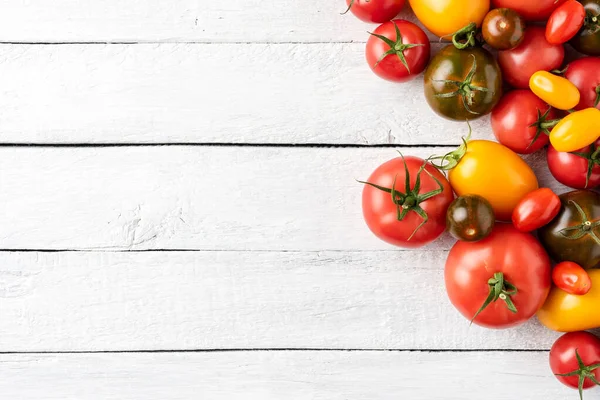 Telif alanı olan beyaz ahşap masadaki çeşitli domateslerin yukarıdan çekimleri. Gıda arkaplanı