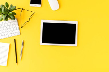 İş aksesuarlarıyla sarı arka planda boş ekranı olan dijital tablet. Ofis masaüstü