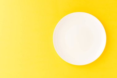 Sarı masada boş beyaz tabak. Üst görünüm