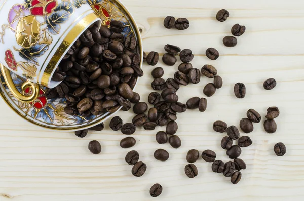 Tazza di caffè in porcellana rovesciata con chicchi di caffè sul tavolo di legno — Foto Stock