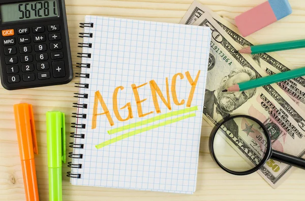 Notebook with agency word and office tools on wooden table