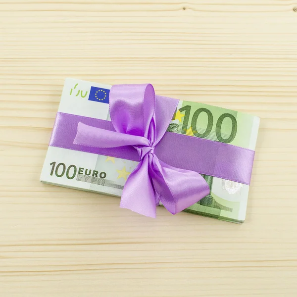 Hundred euro bill with pink bow on wooden table — Stock Photo, Image