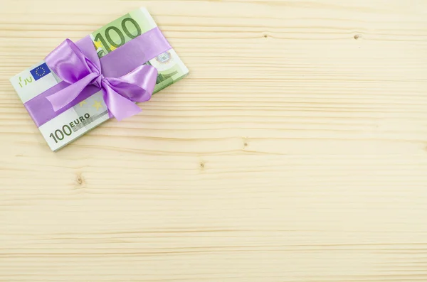 Hundred euro bill with pink bow on wooden table — Stock Photo, Image