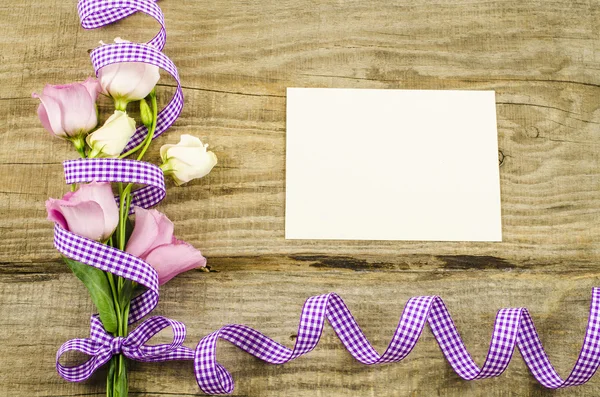 Cartão postal vazio, flor e fita roxa em fundo de madeira — Fotografia de Stock