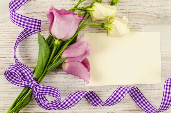 Empty postcard, flower and purple ribbon on wooden background — Stock Photo, Image