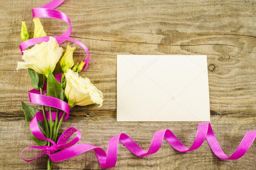Empty postcard, colorful flowers and ribbon on wooden background