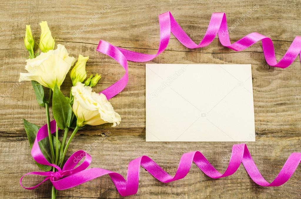 Empty postcard, colorful flowers and ribbon on wooden background