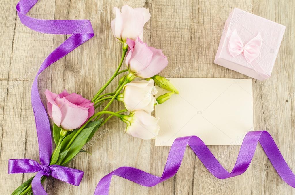 Empty postcard, flower and purple ribbon on wooden background