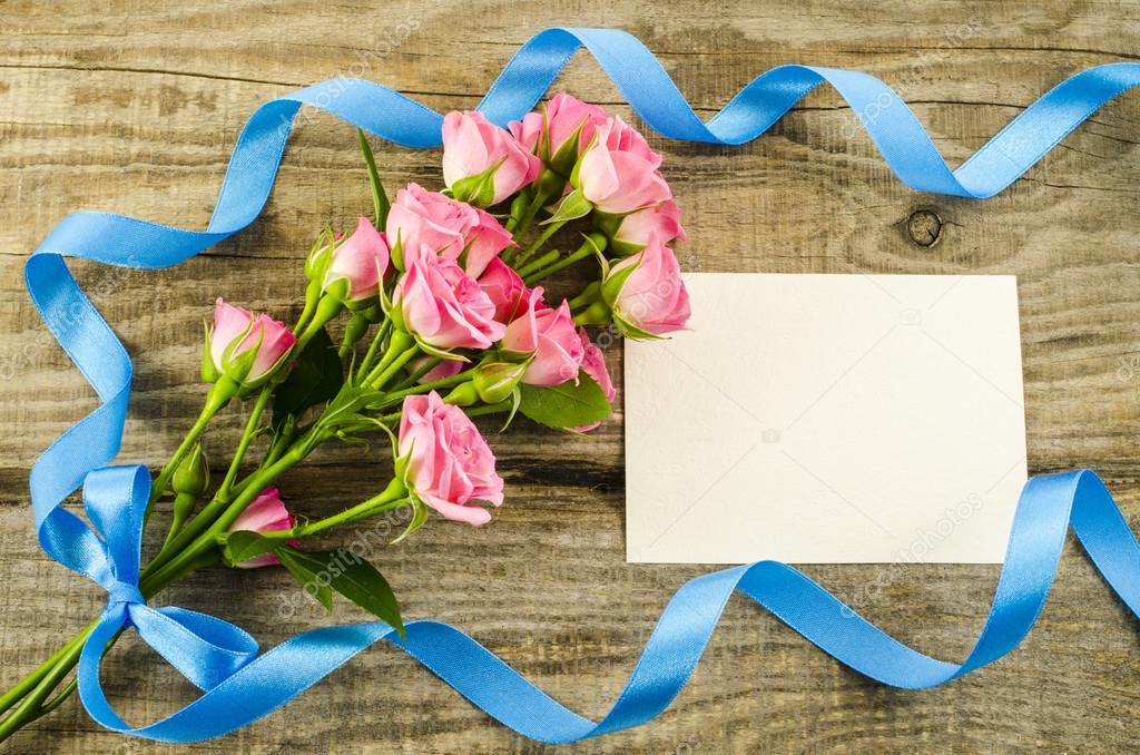 Empty postcard, flower and blue ribbon on wooden background