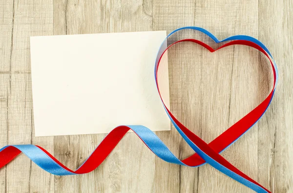 Empty card with heart shaped ribbon on wooden background — Stock Photo, Image