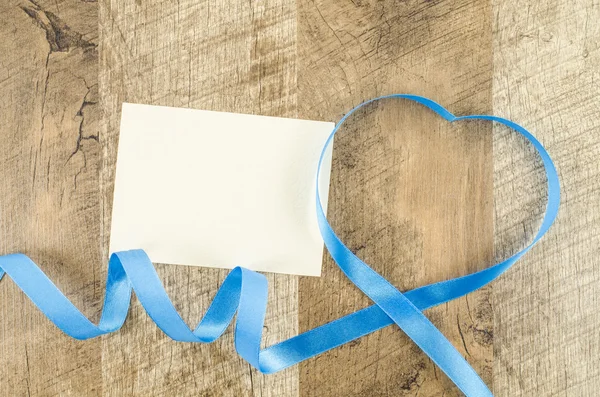 Empty card with heart shaped ribbon on wooden background — Stock Photo, Image