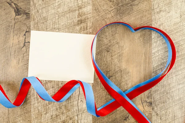 Empty card with heart shaped ribbon on wooden background — Stock Photo, Image
