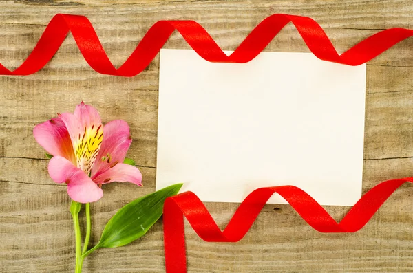 Boş oyun kağıdı, çiçek ve ahşap arka plan üzerinde kırmızı kurdele — Stok fotoğraf