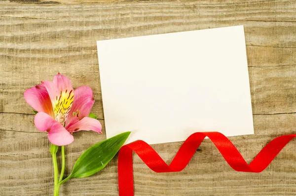 Prázdná karta, květin a červenou stuhou na dřevěné pozadí — Stock fotografie