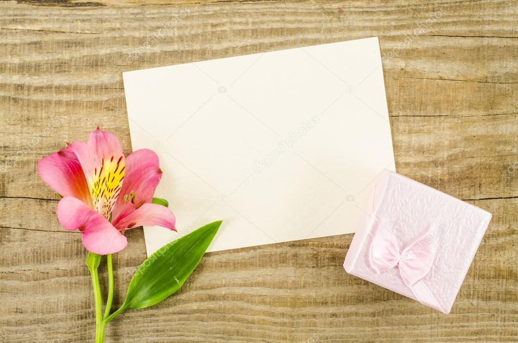 Empty card with gift box and flower on wooden background