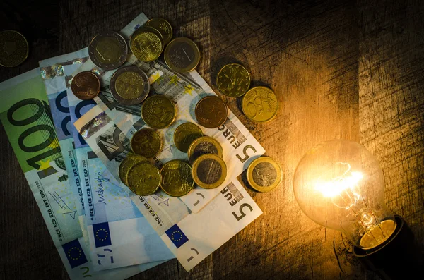 Lampadina incandescente con soldi su sfondo di legno — Foto Stock