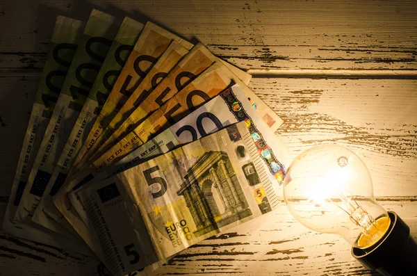 Lampadina incandescente con soldi su sfondo di legno — Foto Stock