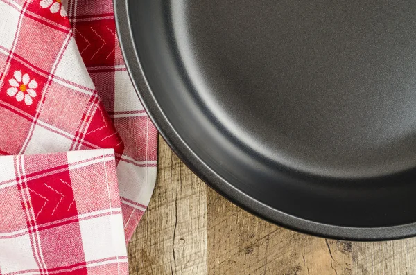 Folded tablecloth and frying pan on white wooden background — Stock Photo, Image