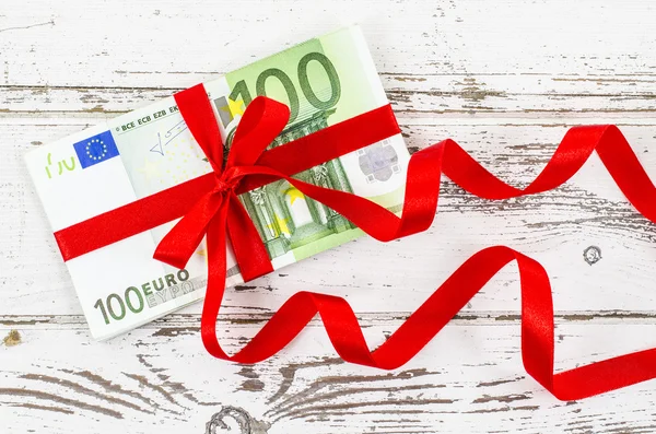 Sto euro účet s červenou stuhou na dřevěný stůl — Stock fotografie