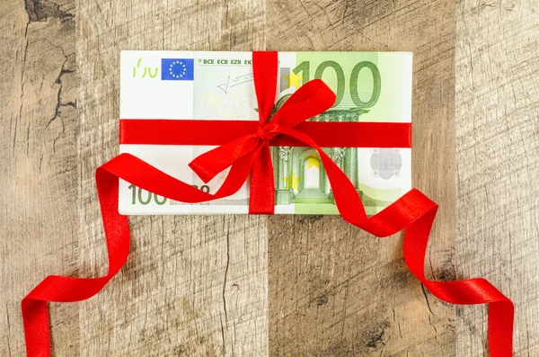 Hundred euro bill with red ribbon on wooden table — Stock Photo, Image