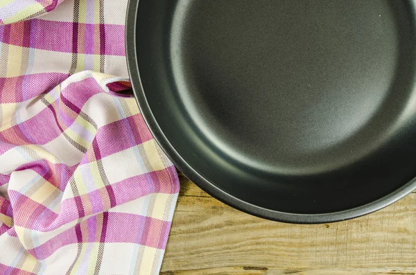 Folded towel with frying pan over wooden table — Stock Photo, Image