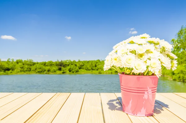 Kbelík plný květin na dřevěný stůl s krajinou — Stock fotografie