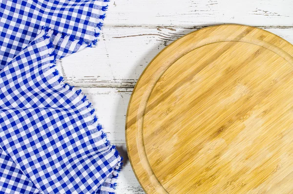 Cutting board with folded tablecloth on white wooden table — Stock Photo, Image