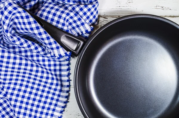 Folded tablecloth and frying pan on wooden background — Stock Photo, Image
