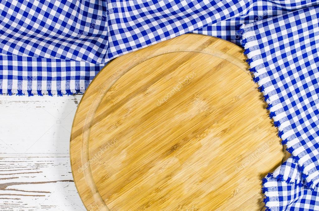 Cutting board with folded tablecloth on white wooden table