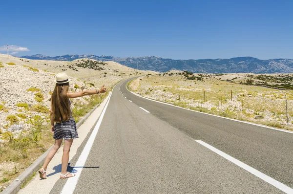 Jovem mulher carona ao longo da estrada vazia — Fotografia de Stock