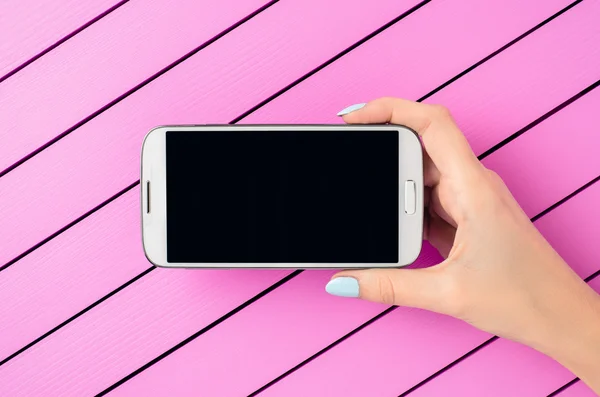 ピンク色の背景に白の携帯電話を保持している女性の手 — ストック写真