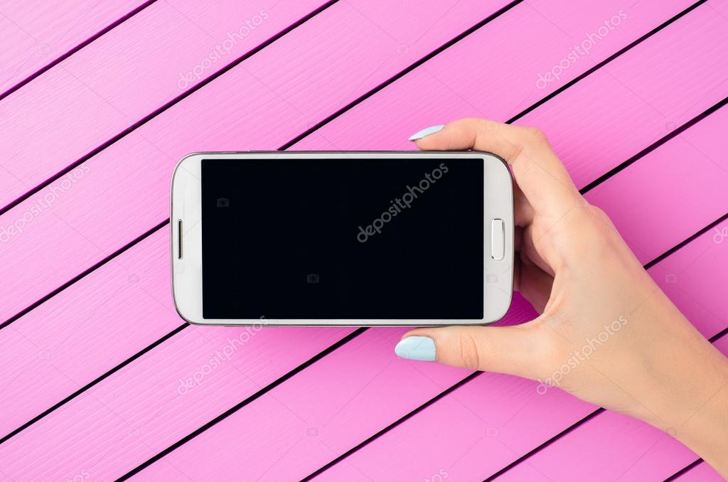 ピンク色の背景に白の携帯電話を保持している女性の手 ストック写真 C Leszekczerwonka