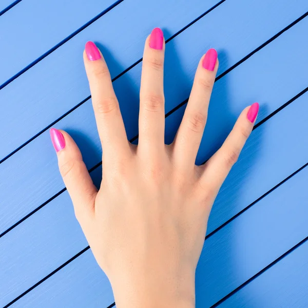 Weibliche Hand mit rosa Nägeln auf blauem Holzhintergrund — Stockfoto