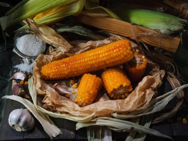 Koyu arkaplanda bulunan tahtanın üzerinde sarımsak ve tuz ile pişirilmiş mısır kulakları.