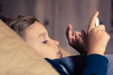 Küçük çocuk yatağa uzanıp, akşamları dijital tablette çizgi film izliyor.. 