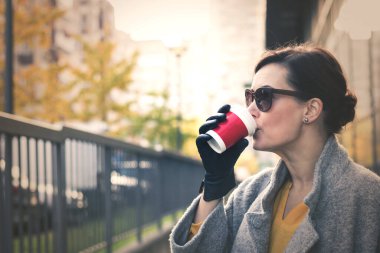 Zarif bir kadın tek kullanımlık fincandan kahve içiyor ve şehirde sonbahar gününün tadını çıkarıyor.. 