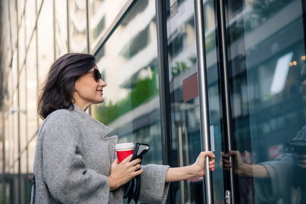 Gülümseyen kadın apartmana giriyor. Mutlu iş kadını işe geliyor ve ofis binasına giriyor..