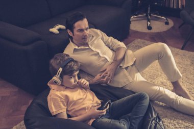 Baba ve oğul evde birlikte dinleniyorlar. Çocuk video oyunu oynarken babası izliyor.. 