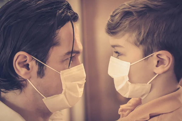 Baba ve oğlunun yüz maskesi taktığı ve Coronavirus salgını sırasında birbirlerine baktıkları yakın çekim.. 