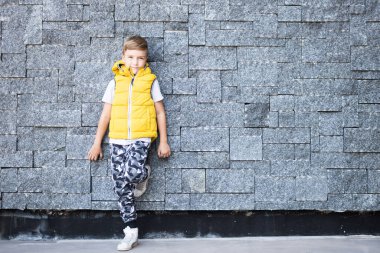 Duvara dayanmış kameraya bakan sevimli bir çocuk. Boşluğu kopyala.