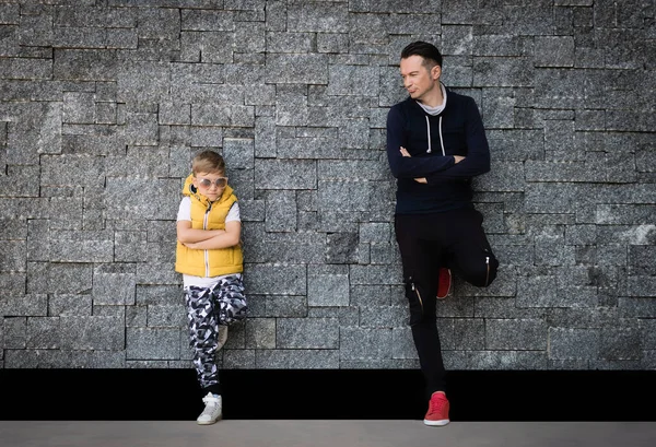 Tuğla duvara yaslanmış çapraz kollu bir baba ve oğul. Boşluğu kopyala.  