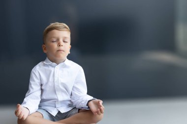 Küçük çocuk nilüfer pozisyonunda yoga yapıyor ve gözleri kapalı meditasyon yapıyor. Boşluğu kopyala.