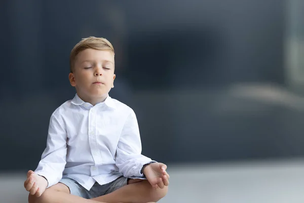 Küçük çocuk nilüfer pozisyonunda yoga yapıyor ve gözleri kapalı meditasyon yapıyor. Boşluğu kopyala.