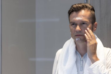 Tıraş olduktan sonra yüz kremi süren bir adamın aynadaki yansıması.. 